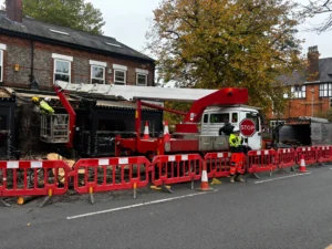Tree surgeon in MEWP dismantling final section of Lime tree with safety barriers and traffic management in place.
